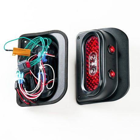 Side-by-side view of the Tail Gunner Tail Light for Jeep JK, showcasing the back wiring components on the left and the fully assembled light with its red lens on the right. The left section displays a network of colorful wires and a resistor module within the black powder-coated aluminum housing. The right section highlights the sleek, completed design with two integrated red side marker lights and a reflective red tail light lens.
