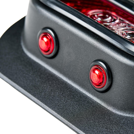 Close-up detail of the Tail Gunner Tail Light for Jeep JK, highlighting two bright red side marker lights embedded in the black powder-coated aluminum housing. The smooth surface and precise construction emphasize the light's durability and premium finish. The edge of the main tail light lens is visible in the upper background.
