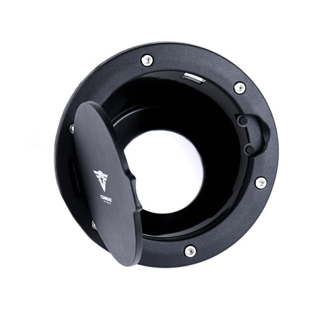 A black Combat Off Road fuel door cover for Jeep JK shown with the door open, revealing the fuel compartment. The cover features a textured finish, stainless steel bolt accents, and the Combat Off Road logo in white on the interior of the door. Designed for durability and a rugged aesthetic, this cover enhances both function and style.