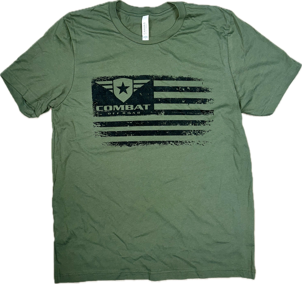A green t-shirt featuring a distressed black design of the Combat Off Road logo integrated into a stylized American flag. The logo, placed in the top left corner of the flag, includes a shield with a star and winged accents, accompanied by the text "Combat Off Road" in bold black letters. The shirt has a classic crewneck and short sleeves, offering a casual and rugged look.