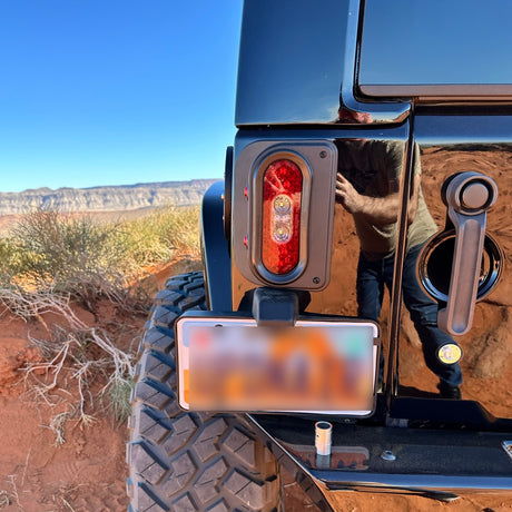 Rear view of a Jeep JK fitted with a Tail Gunner Tail Light. The black aluminum housing encases a bright red LED main light with two additional red side markers. The Jeep is showcased showcased in an off-road environment with desert terrain in the background. The tail light complements the rugged styling and functionality of the Jeep.