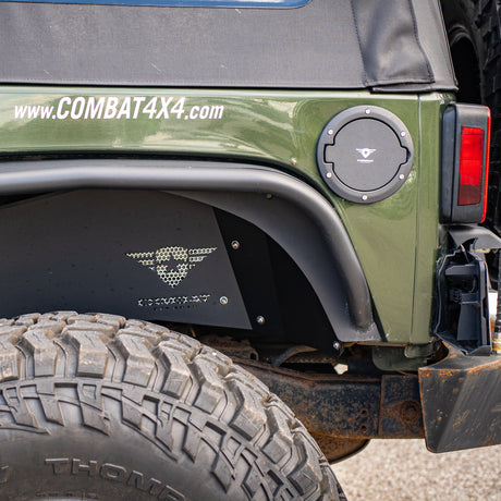 A Jeep JK showcasing a black Combat Off Road fuel door cover with a textured finish, stainless steel bolt accents, and the Combat Off Road logo in white at the center. Below the fuel door, the Jeep is equipped with black Combat Off Road rear inner fender liners featuring a laser-cut logo and mesh ventilation. The vehicle's green body is highlighted, along with the website URL "www.COMBAT4X4.com" on the upper body panel and an aggressive off-road tire in the foreground.